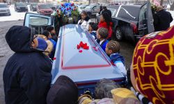 Many people are carrying a casket and putting it in a hearse. 