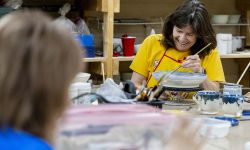Margaret Afheldt smiles as she glazes a bowl. 