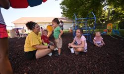 Children and adults sit on the ground at a playground
